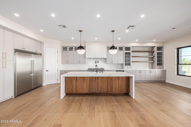 kitchen with visible vents, stainless steel built in fridge, open shelves, a center island with sink, and light wood-style flooring