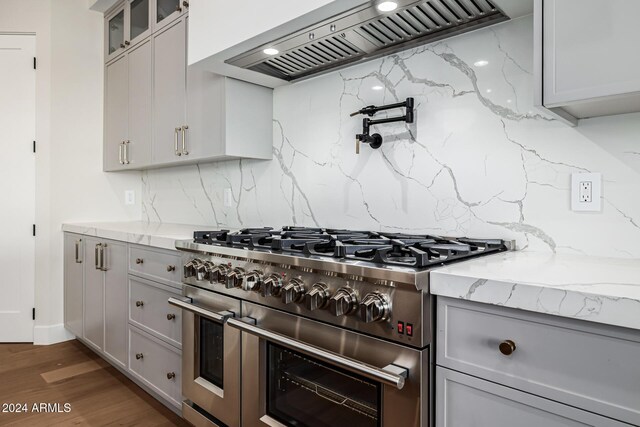 kitchen with light stone counters, range with two ovens, tasteful backsplash, gray cabinetry, and custom exhaust hood