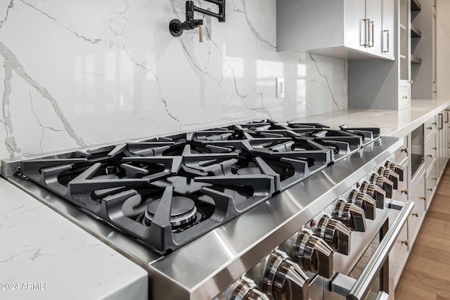 interior details featuring stovetop, tasteful backsplash, open shelves, light stone counters, and white cabinetry