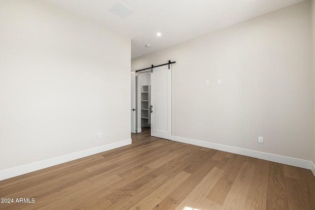 unfurnished bedroom with baseboards, a barn door, light wood finished floors, and visible vents