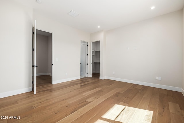 unfurnished bedroom featuring light wood-style floors, baseboards, recessed lighting, and a spacious closet