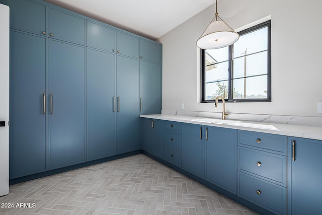 kitchen with a sink, light stone countertops, blue cabinets, and decorative light fixtures