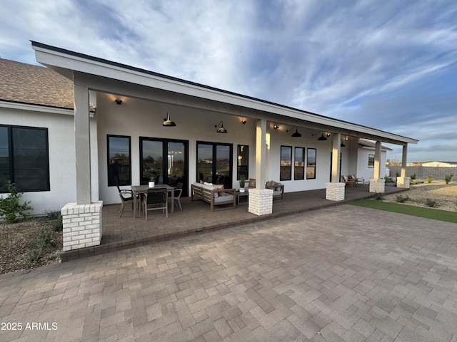 back of house with a patio, outdoor lounge area, stucco siding, and roof with shingles