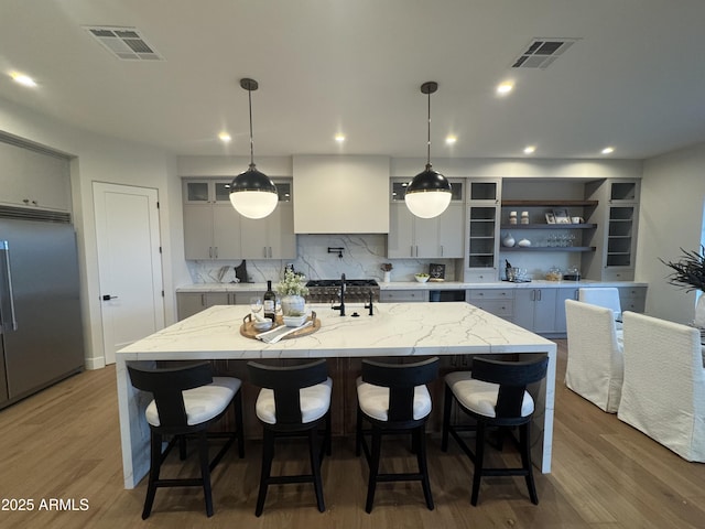 kitchen with a center island with sink, stainless steel built in refrigerator, wood finished floors, and visible vents