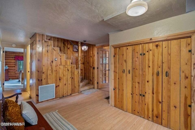 interior space featuring stairs, wood finished floors, a textured ceiling, wood walls, and visible vents
