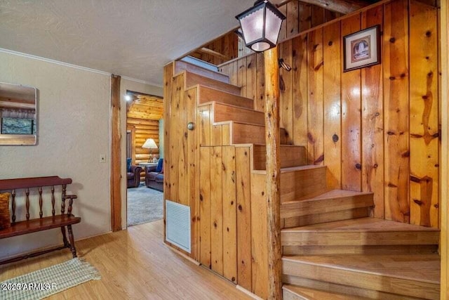 staircase featuring wood finished floors, visible vents, wood walls, and ornamental molding
