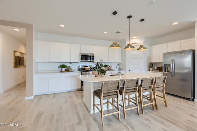 kitchen featuring appliances with stainless steel finishes, a kitchen island with sink, light countertops, pendant lighting, and a sink