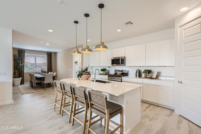 kitchen with a center island with sink, visible vents, appliances with stainless steel finishes, light countertops, and a sink