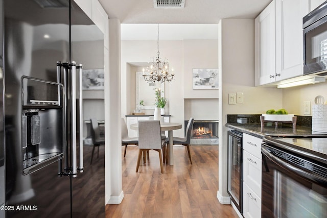 kitchen with black appliances, dark countertops, beverage cooler, and white cabinets