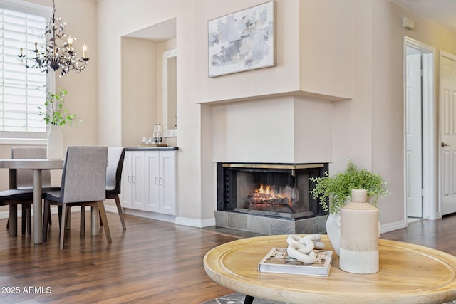 living room with wood finished floors, a tiled fireplace, a chandelier, and baseboards