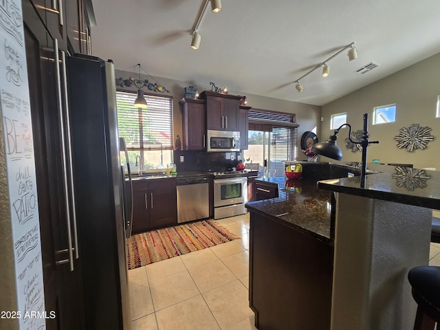 kitchen with light tile patterned flooring, vaulted ceiling, backsplash, dark brown cabinetry, and stainless steel appliances