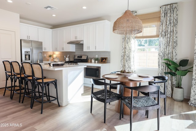 kitchen featuring white cabinets, a center island with sink, stainless steel appliances, and hanging light fixtures