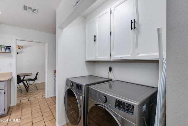 laundry area with washing machine and dryer, light tile patterned floors, and cabinets