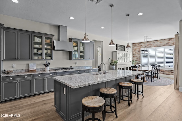 1439 E Mead Dr, Gilbert, AZ 85298 - kitchen with a sink, brick wall, light wood-style flooring, wall chimney range hood, and a breakfast bar