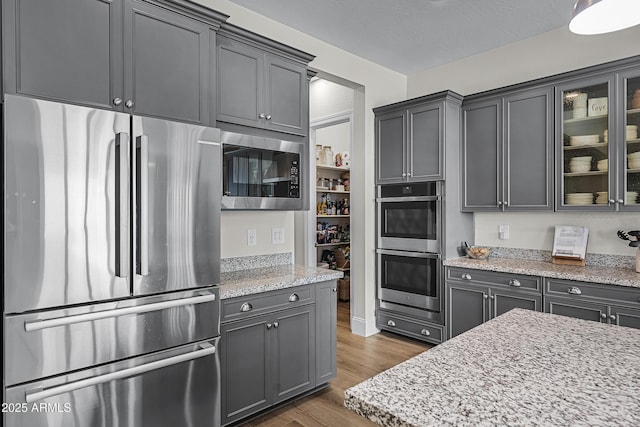 1439 E Mead Dr, Gilbert, AZ 85298 - kitchen with stainless steel appliances, wood finished floors, glass insert cabinets, light stone counters, and gray cabinets