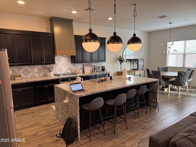 kitchen with premium range hood, visible vents, wood finished floors, and a sink