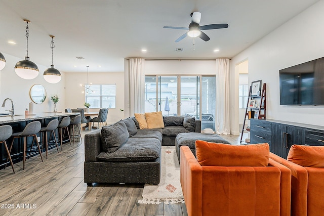 living room featuring ceiling fan with notable chandelier, light wood-style flooring, recessed lighting, and visible vents