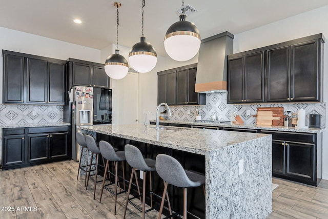 kitchen with custom range hood, visible vents, light wood finished floors, and a sink