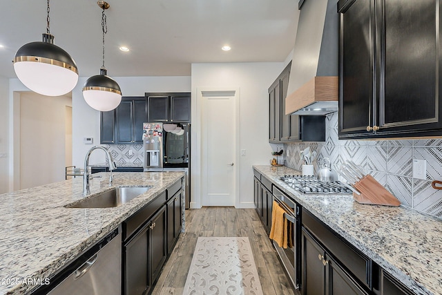 kitchen featuring light stone countertops, premium range hood, stainless steel appliances, a sink, and light wood-type flooring