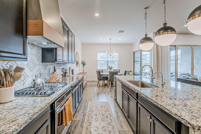 kitchen with premium range hood, oven, a sink, light wood finished floors, and stainless steel gas cooktop