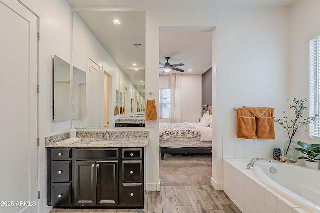 ensuite bathroom with a ceiling fan, wood finished floors, ensuite bath, a bath, and vanity