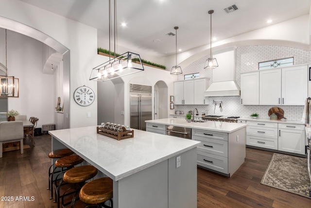 kitchen with visible vents, arched walkways, a kitchen island with sink, dark wood-style flooring, and stainless steel appliances