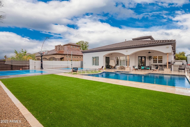 rear view of property featuring fence, a tile roof, a yard, a patio area, and a ceiling fan