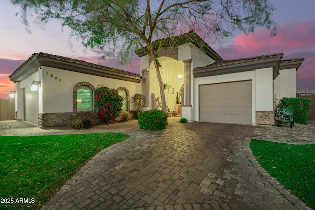 mediterranean / spanish house featuring decorative driveway, stone siding, an attached garage, and a tiled roof