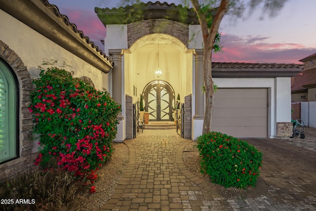 exterior entry at dusk featuring decorative driveway, a garage, and stucco siding