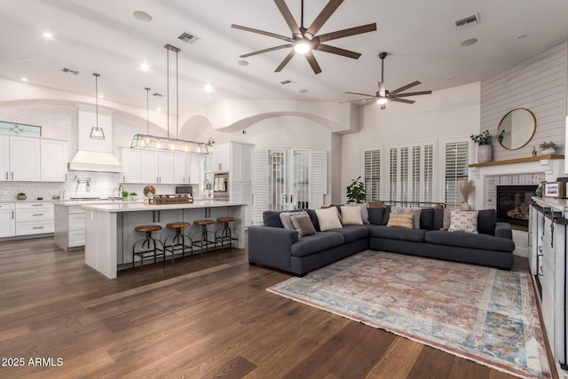 living room with dark wood-style floors, visible vents, a fireplace, and ceiling fan