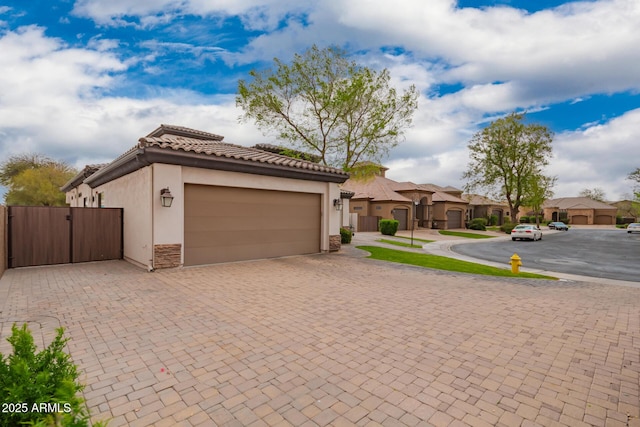 mediterranean / spanish-style home featuring stone siding, decorative driveway, a garage, and a gate