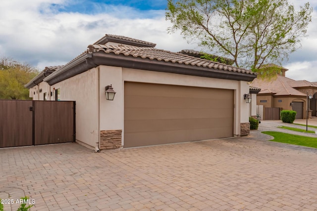 exterior space featuring decorative driveway, stone siding, fence, and a tile roof