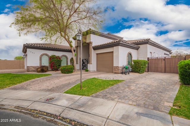 mediterranean / spanish home featuring a gate, an attached garage, stucco siding, a tile roof, and decorative driveway