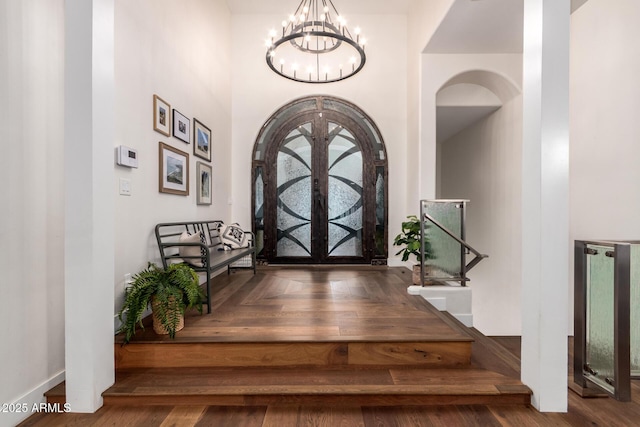 entrance foyer featuring a chandelier, french doors, a high ceiling, wood finished floors, and arched walkways