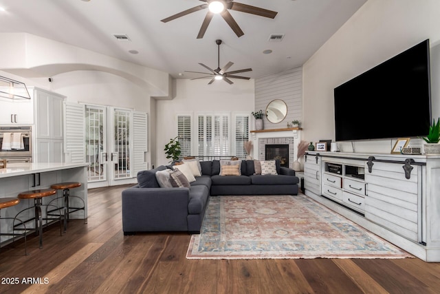 living room with dark wood finished floors, a brick fireplace, a ceiling fan, and visible vents