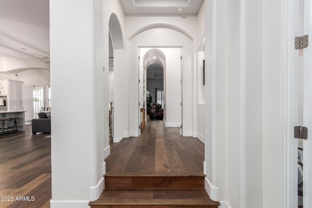 hallway with arched walkways, dark wood-style floors, and baseboards