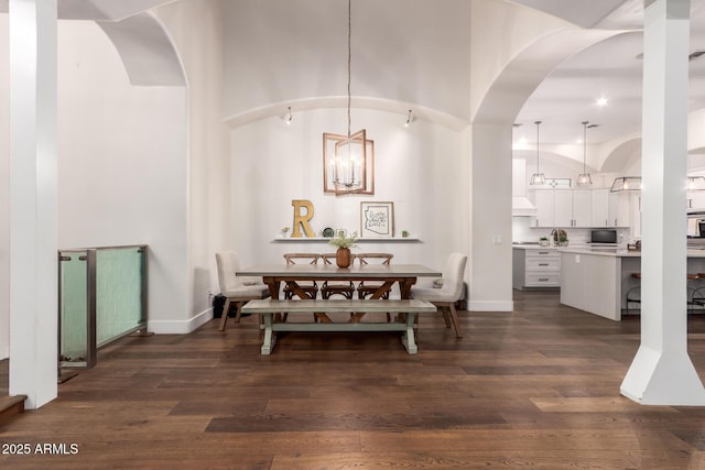 dining space featuring arched walkways, dark wood finished floors, an inviting chandelier, and a towering ceiling