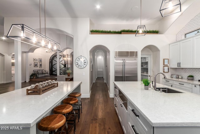 kitchen with a spacious island, built in fridge, arched walkways, and a sink