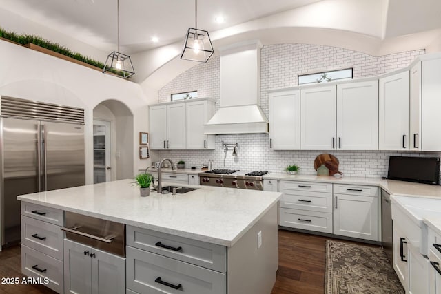 kitchen with dark wood-style floors, appliances with stainless steel finishes, arched walkways, custom exhaust hood, and a sink