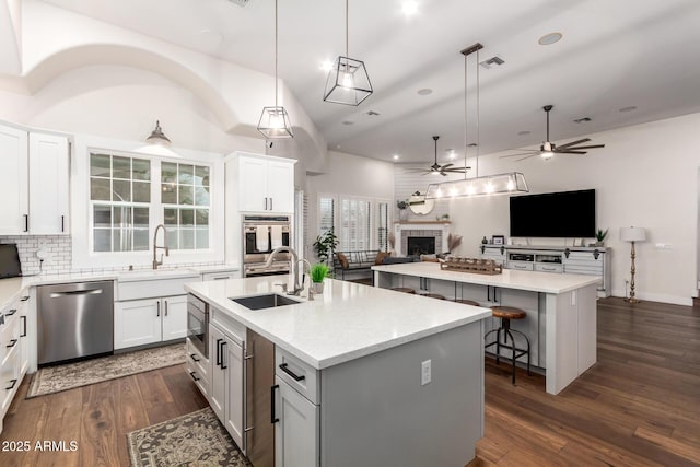 kitchen featuring a kitchen island with sink, open floor plan, a fireplace, stainless steel appliances, and a sink