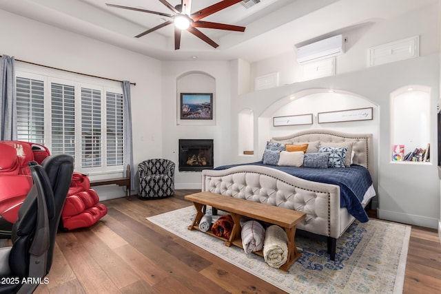 bedroom featuring visible vents, a raised ceiling, an AC wall unit, hardwood / wood-style flooring, and baseboards