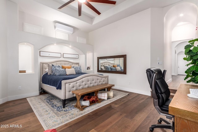 bedroom featuring a wall mounted air conditioner, arched walkways, a raised ceiling, and wood finished floors