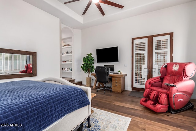 bedroom featuring a ceiling fan, wood finished floors, baseboards, a tray ceiling, and access to outside