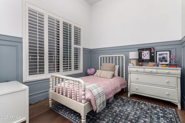 bedroom featuring dark wood-type flooring, a decorative wall, and a wainscoted wall