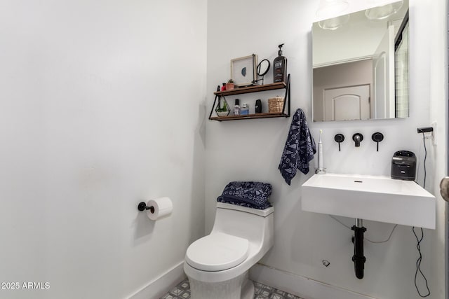 bathroom featuring toilet, baseboards, and a sink