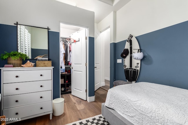 bedroom with a spacious closet, wood finished floors, and a closet