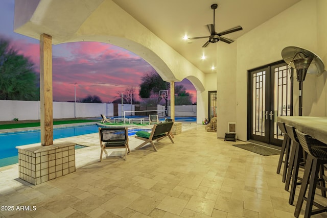 patio terrace at dusk with ceiling fan, a fenced in pool, and a fenced backyard