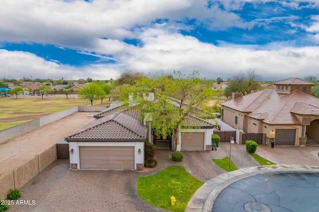 mediterranean / spanish house with a tiled roof, an attached garage, fence, and stucco siding