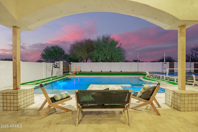 pool at dusk with a patio, a trampoline, a fenced backyard, and a fenced in pool