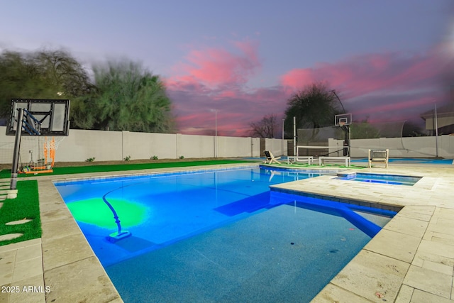 pool at dusk featuring a fenced in pool, an in ground hot tub, and a fenced backyard